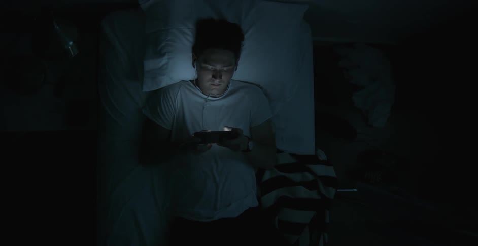 A man plays on his phone in bed in a dark room