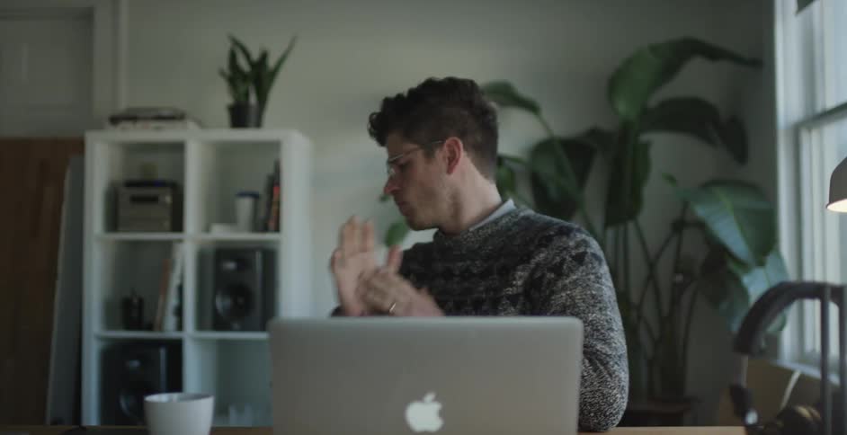 A man wearing glasses sits down and opens a laptop