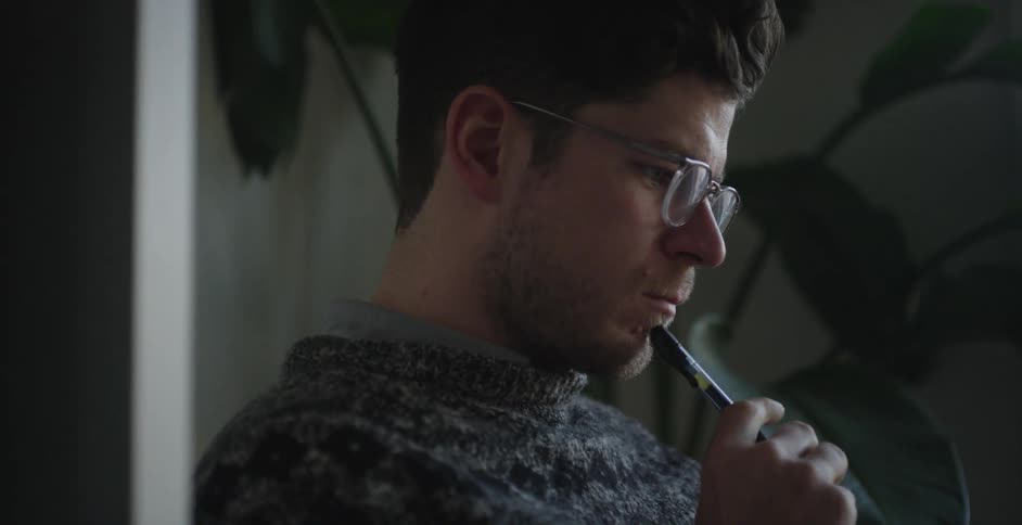 A man puts a pen to his chin as he looks down in a room