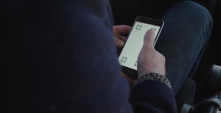 A seated man swipes the screen of a smartphone
