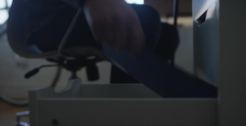 A person in a gray sweater pulls open a drawer and pulls out a book