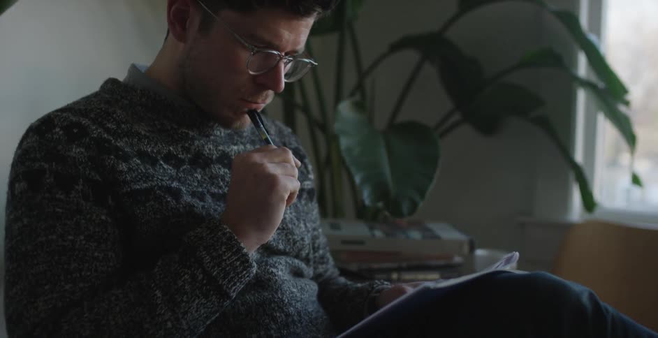 A man in a gray sweater reads and makes notes on some papers