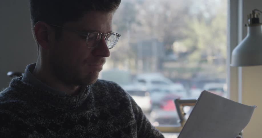 Man reading papers by a window on a sunny day