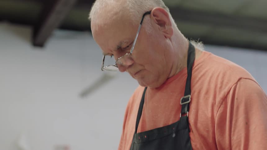 Older man cutting glass at work station