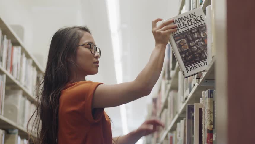 Woman reaching to grab a book on library shelf