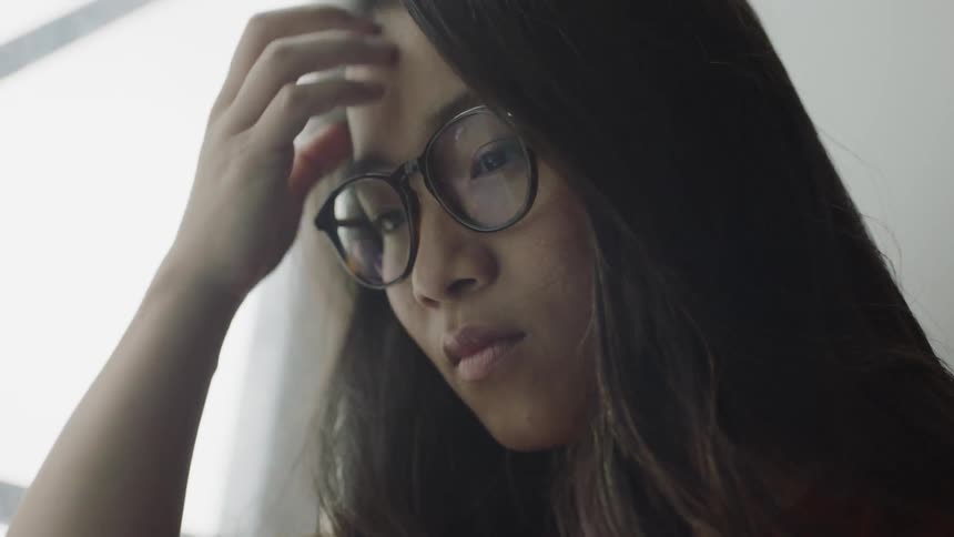 Asian woman touching glasses and hair while looking down