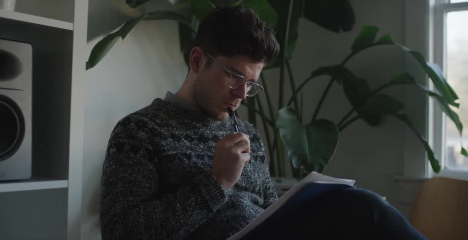 A man in a gray sweater puts a pen to his lips