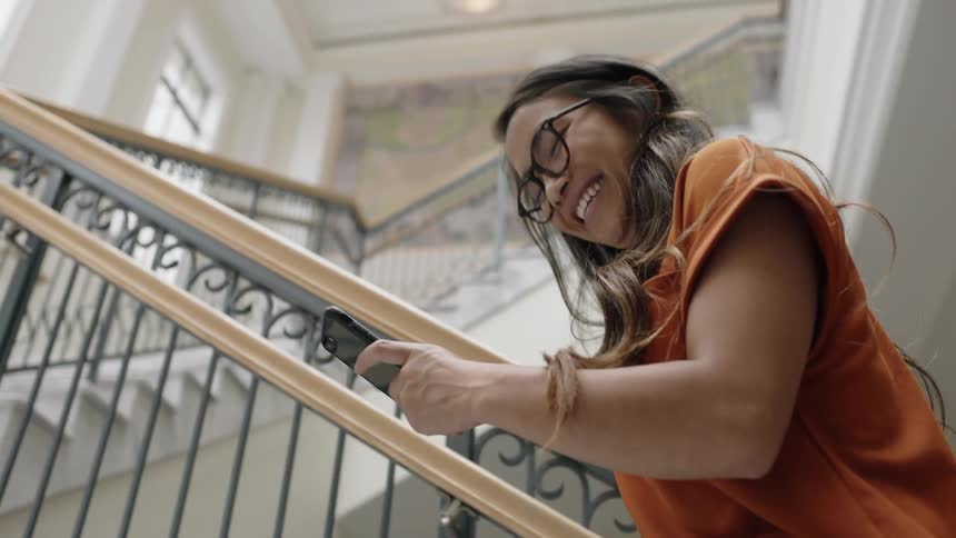 Young woman using phone and walking up stairs