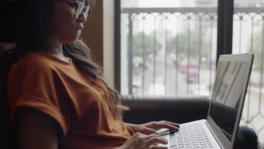 Asian woman typing on silver laptop on chair
