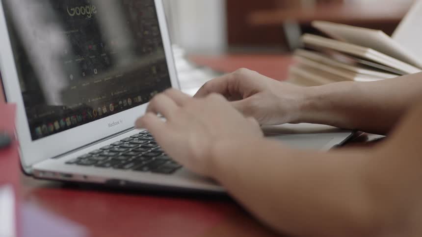 Typing on silver computer at table surrounded by books
