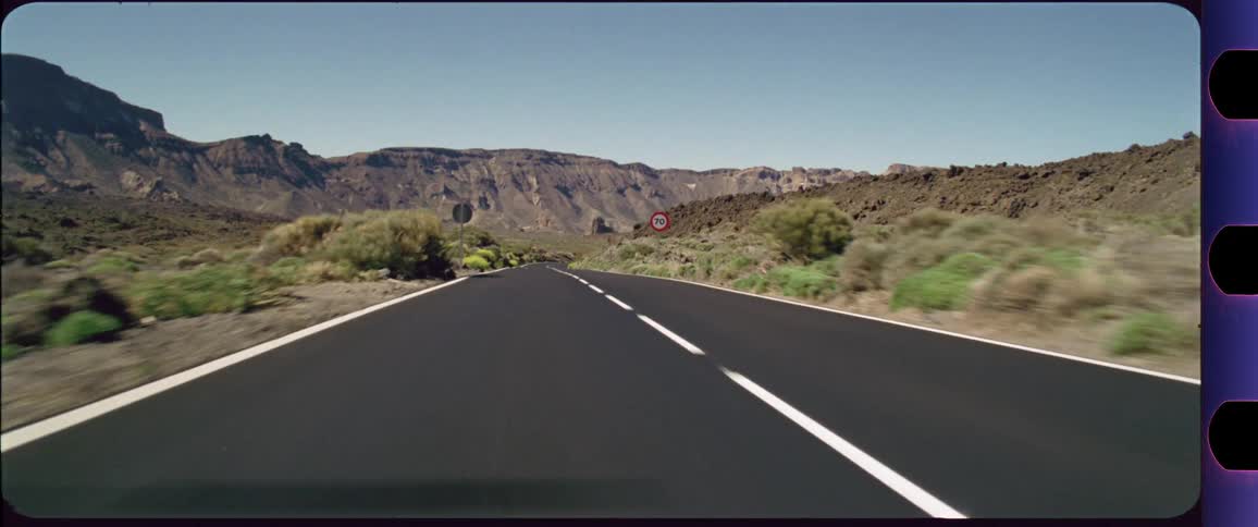 Camera flying above a desert highway with mountains in the background