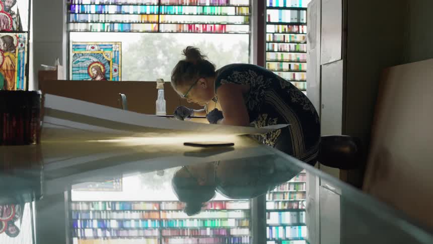 Woman leaning over artwork with stain glass window behind her