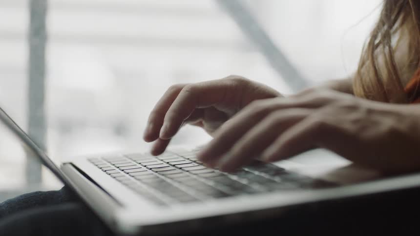 Typing on laptop in front of window