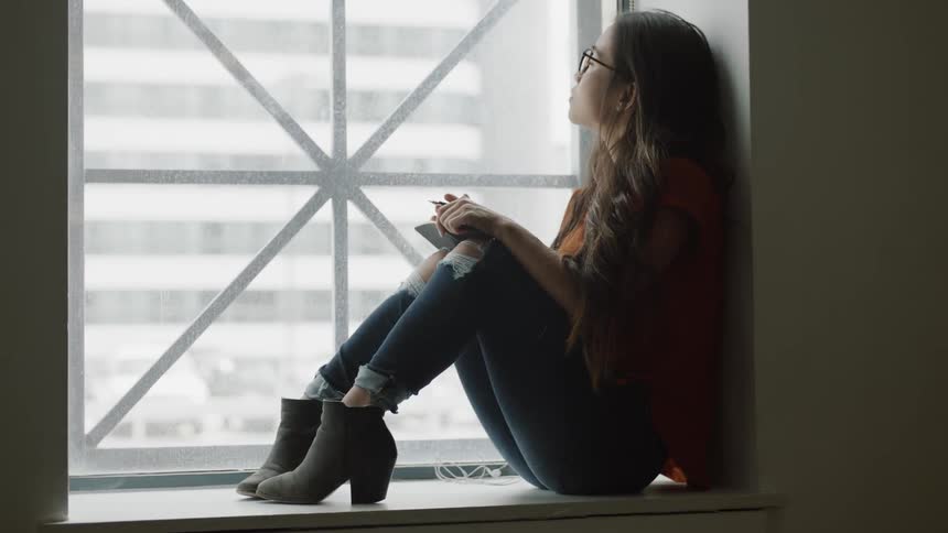 Woman looking out window then writing in notebook