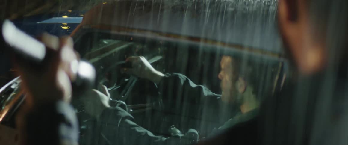 Man walking outside at night in the rain and shines a flashlight on a stopped vehicle