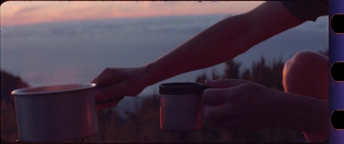 Man drinking coffee from a cup then pouring some more while overlooking perfect sunrise on top of a mountain