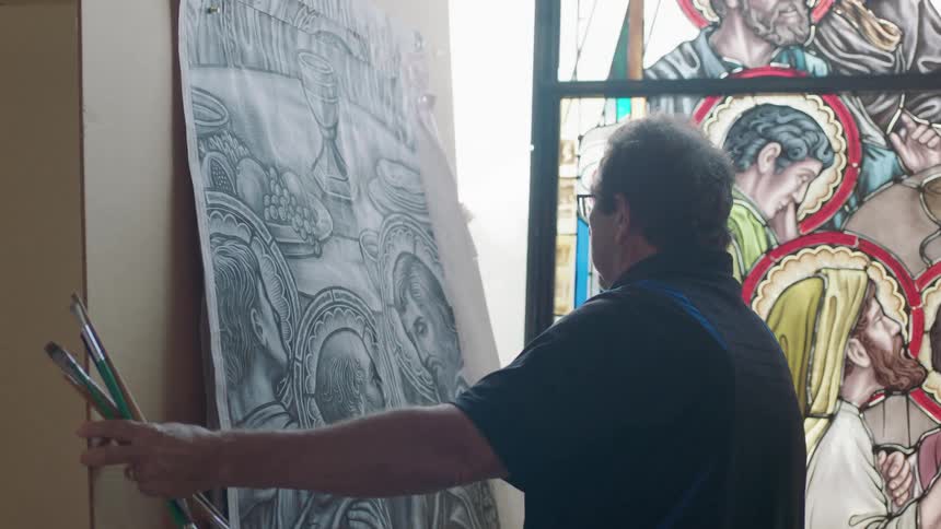 Artist holding paint brushes moving canvas in front of stain glass window