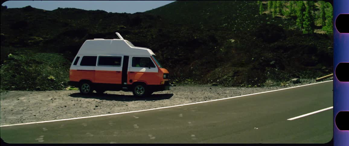 Couple jumping into an old orange VW Bus next to a desert highway