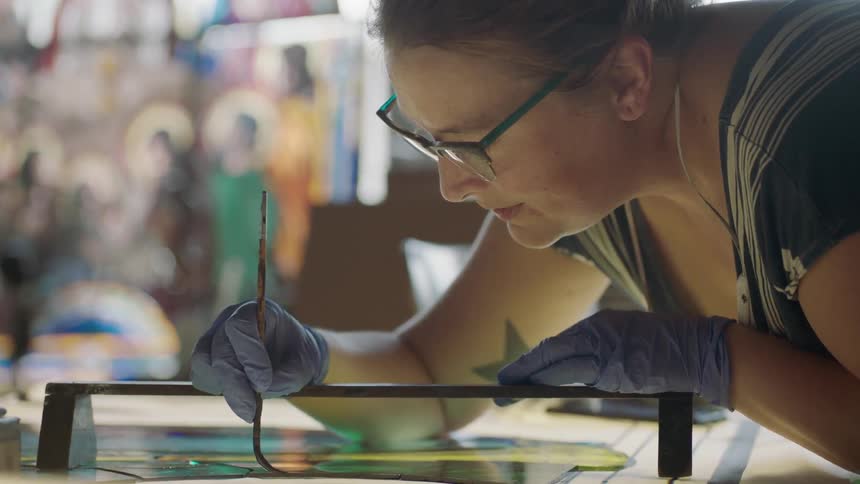 Artist bend over artwork with paint brush in gloved hand