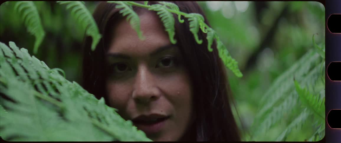 Woman slowly looking up and smiling while standing in between fern