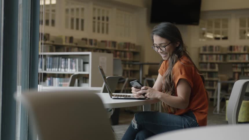 Student smiling at phone at a library