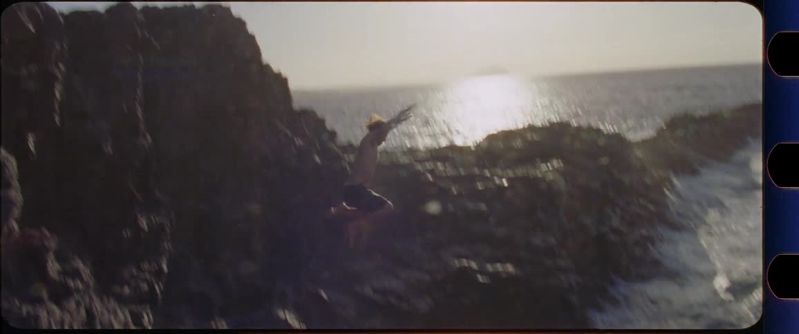 Man jumps off a cliff into the ocean while the sun is setting