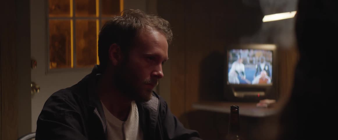 Men smoking at a table with a television playing in the background