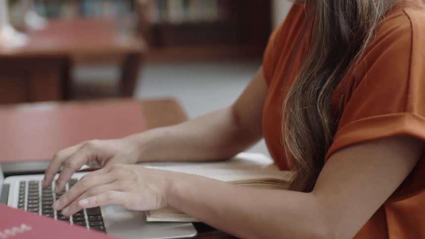 Girl typing computer at table in library