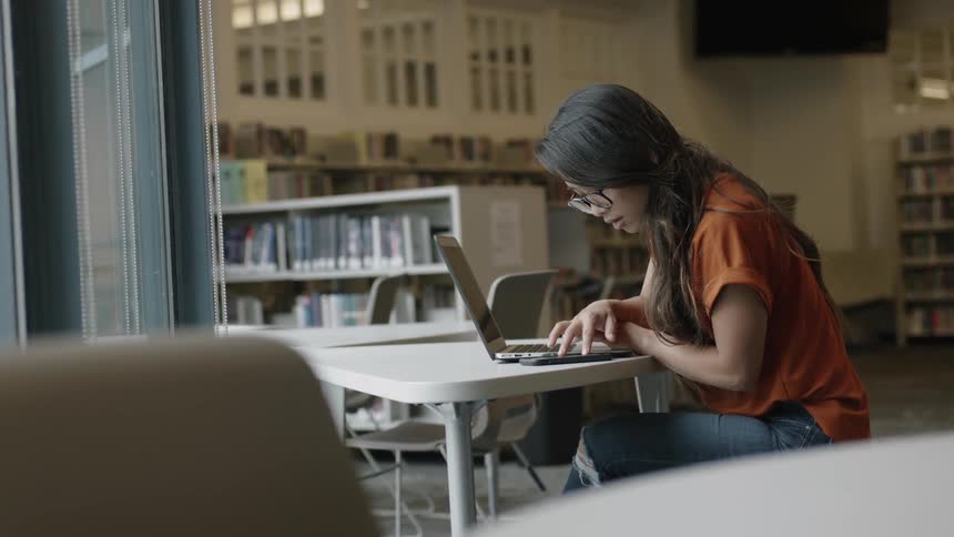 Young woman using phone at table in library