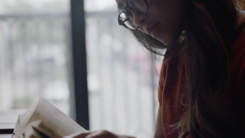 Student reading book in front of large window