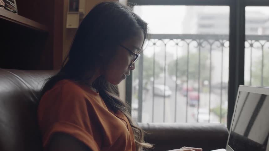 Young adult working on laptop inf ront of large window