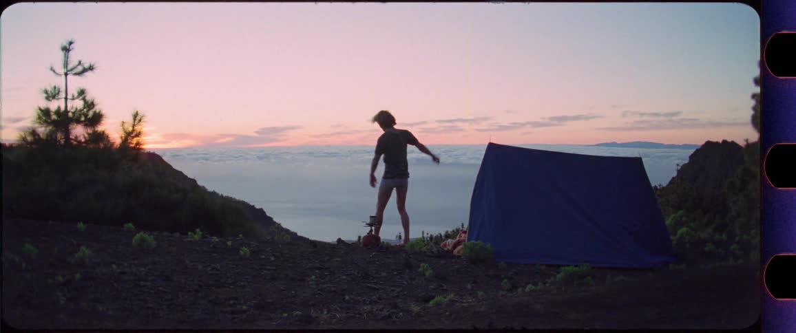 Man stretching in front of his tent on top of a mountain at sunrise overlooking the clouds then starts a cooking a coffee