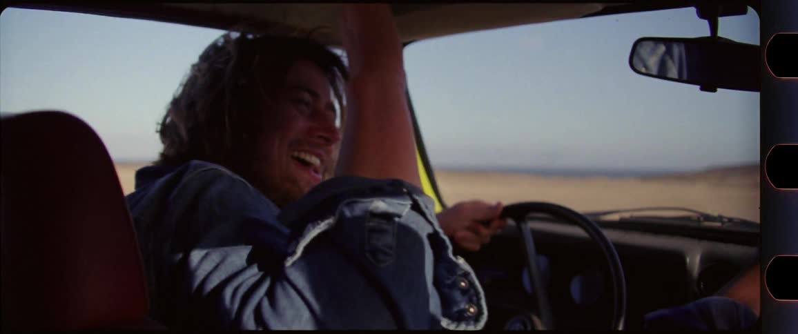 Man sticking his head out the window and giving highfives while driving through beach scenery