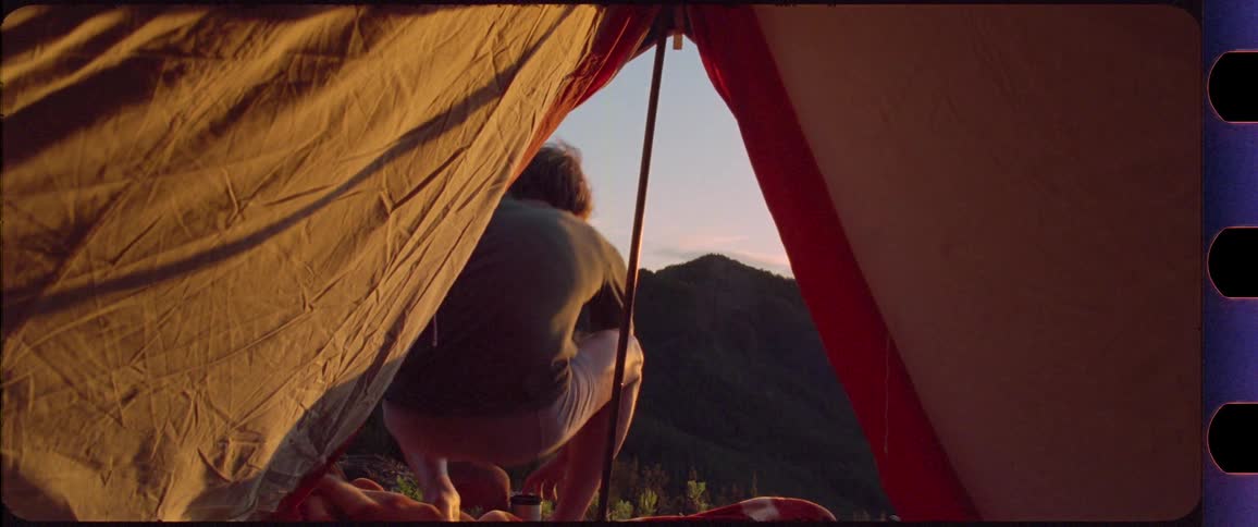 Man opening his tent revealing a mountain sunrise scenery
