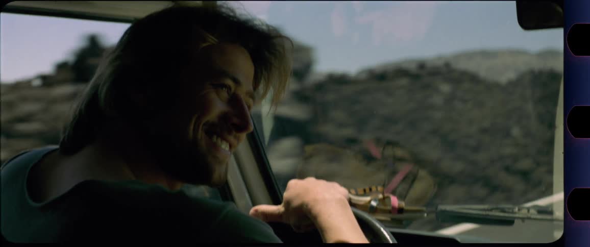 Man smiles to the right while driving a car through desert region