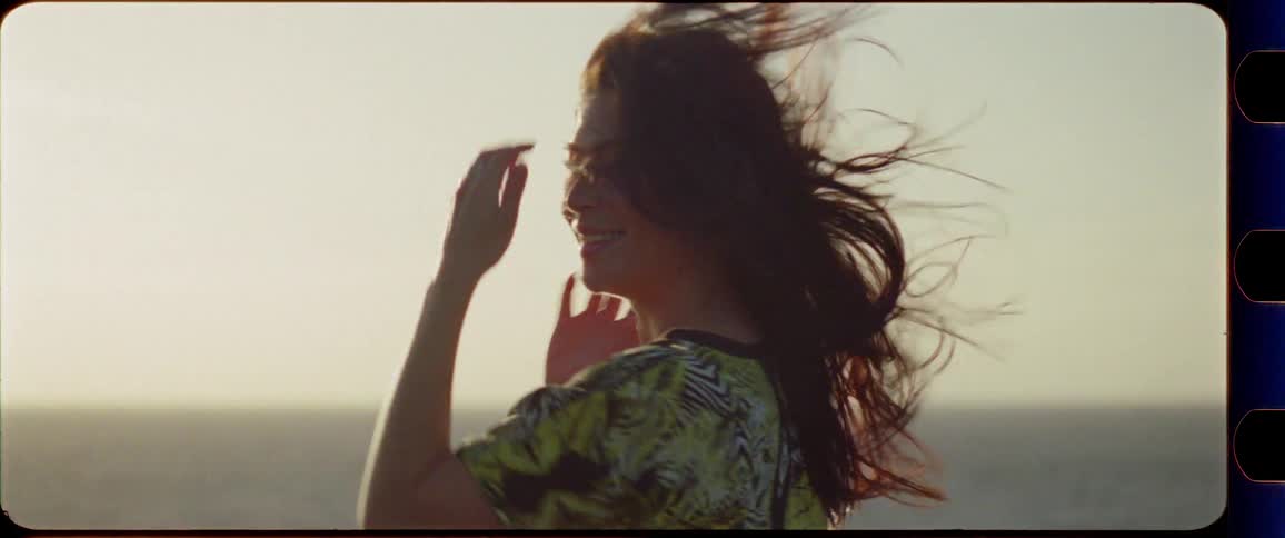 Woman enjoys the sunset by the ocean with wind in her hair smiling to the camera