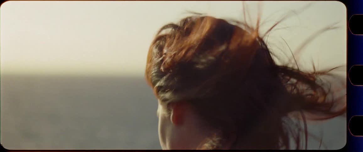 Woman smiles and enjoys the sunset by the ocean with wind in her hair