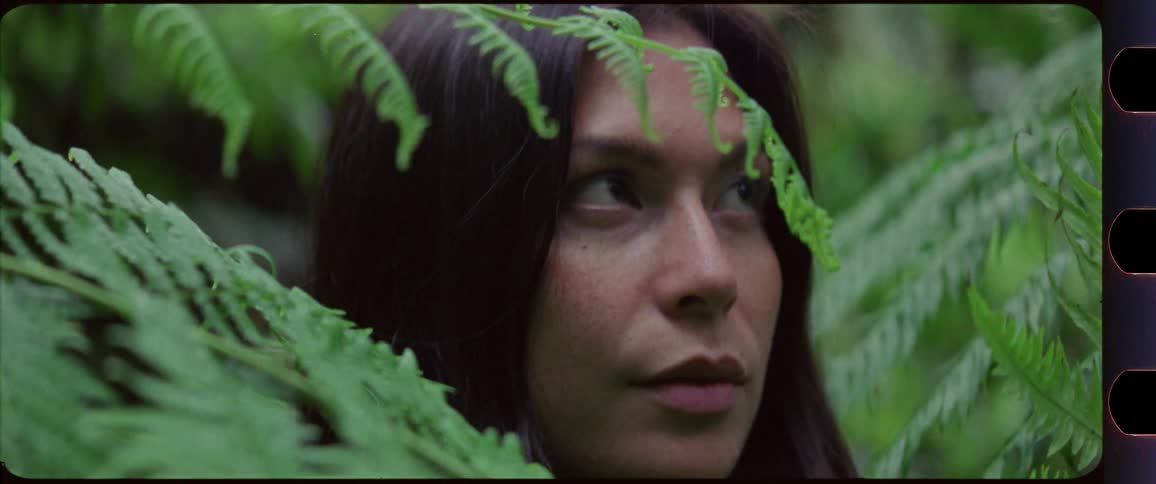 Woman slowly looking up while standing in between fern