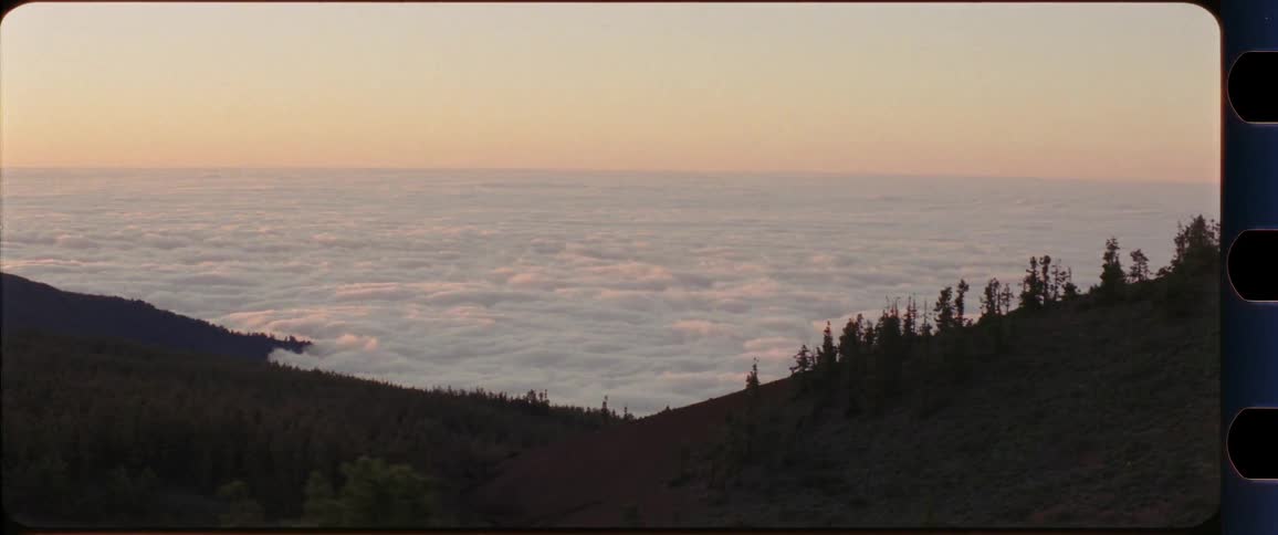 Sea of clouds with mountain region in the foreground shot out of a driving car at sunset