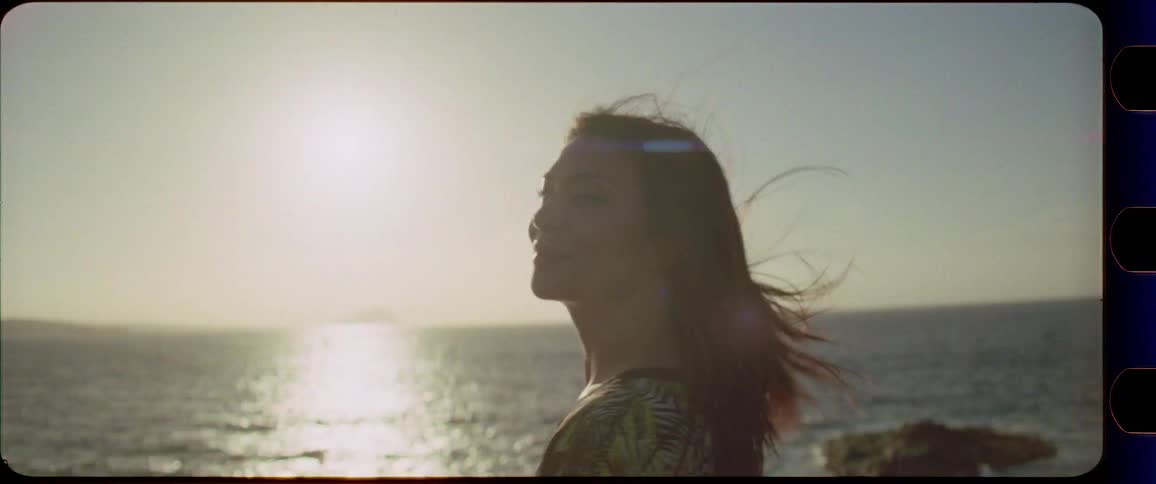 Woman rises her hands and enjoys the sunset by the ocean with wind in her hair