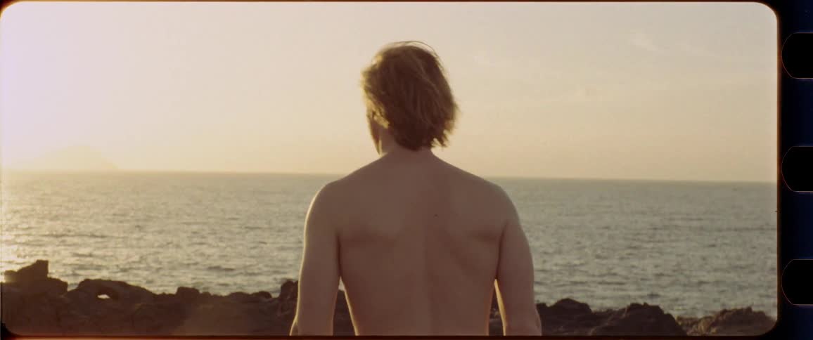 Topless guy watching sunset at the coastline
