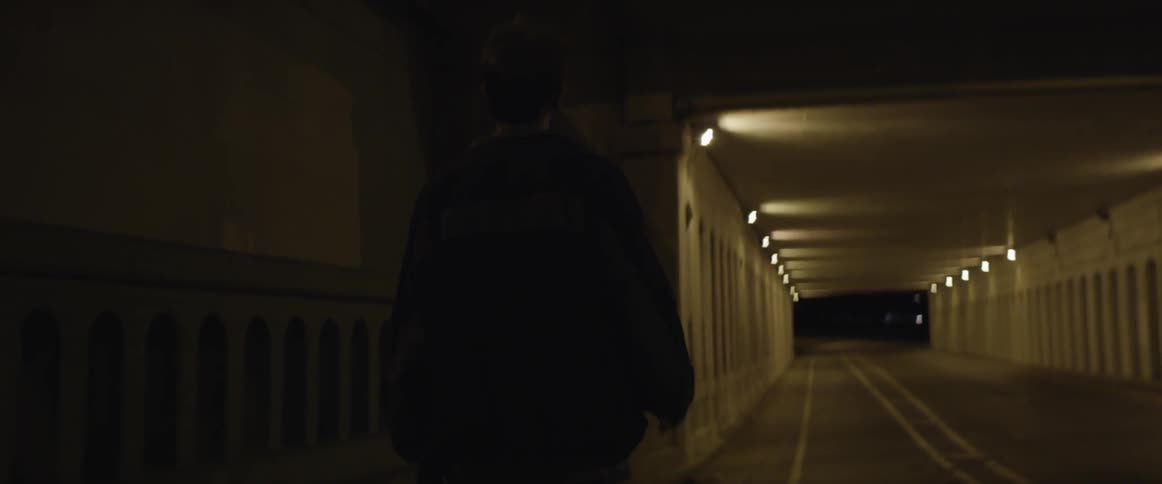 A man walking in the dark towards a lit tunnel