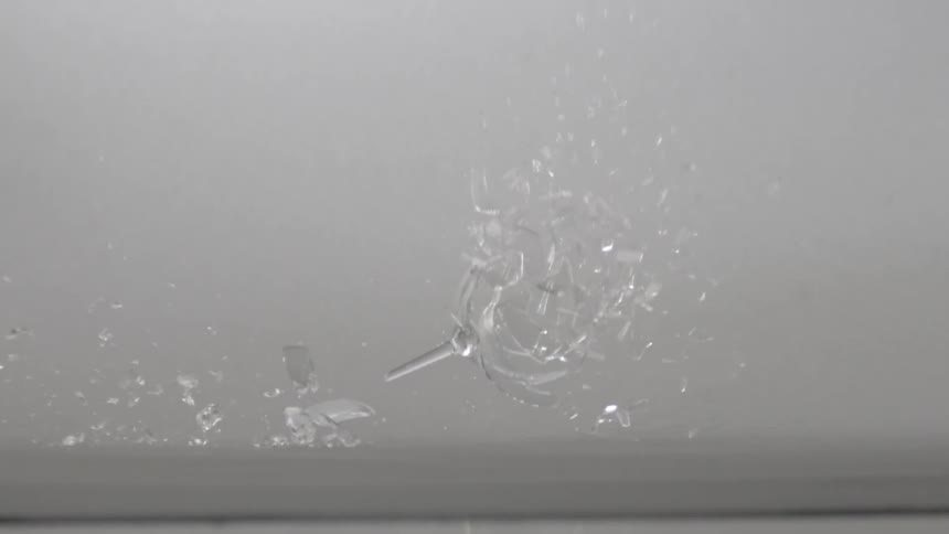 A wine glass hits the surface and shatters