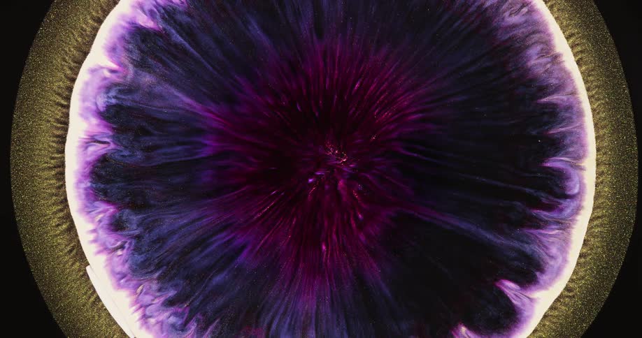 A drop of purple ink spreads out in a golden liquid