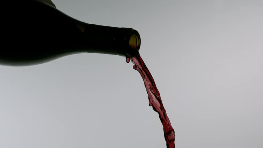 Red wine is poured from a brown bottle