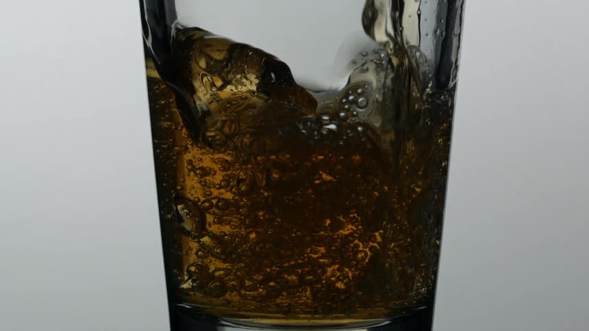 Brown liquid pouring into a glass filling it