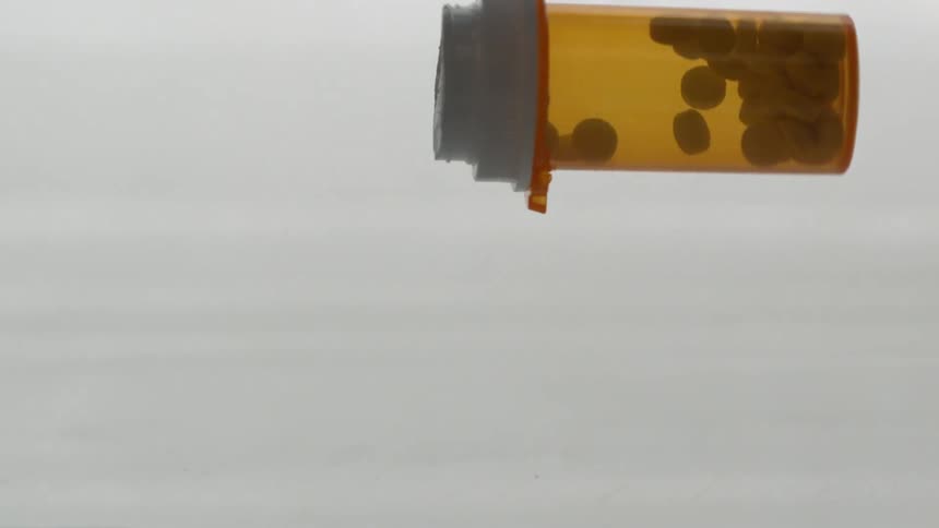A prescription bottle of pills falls and hits a surface without opening