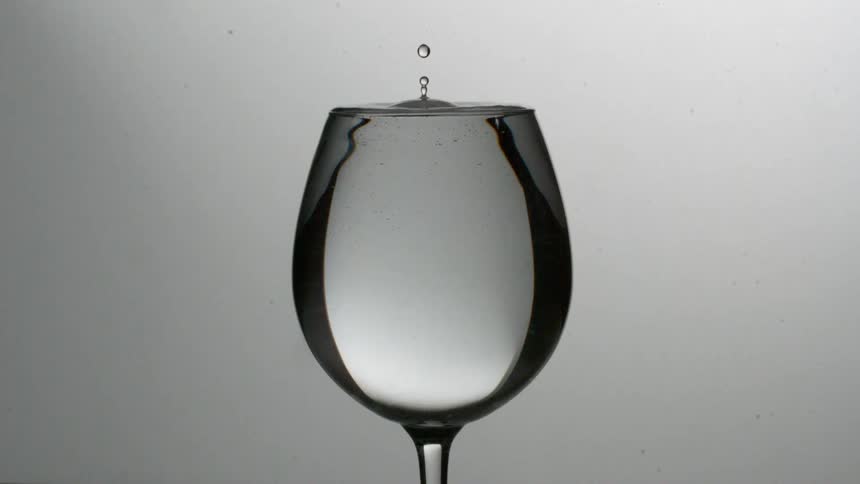 A drop of water falls slowly into a full wine glass