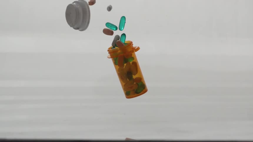 A bottle of pills falls onto a surface and various pills fall out