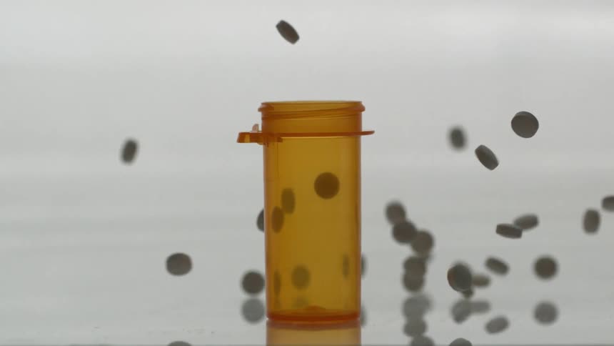 Pills drop in and around a pill bottle